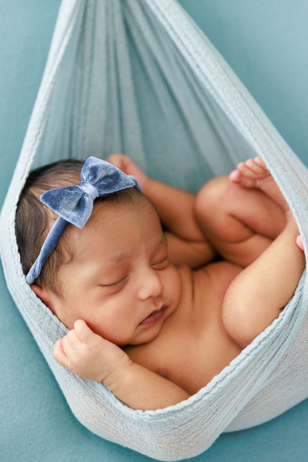 Sleeping newborn in light blue hammock wearing matching bow headband.