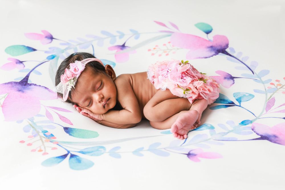 A sleeping newborn with pink accessories lies on a watercolor-style floral backdrop.