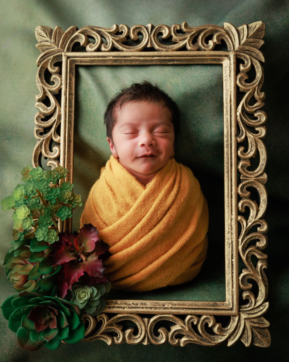 A sleeping newborn wrapped in yellow fabric rests within an ornate gold frame with succulent decorations.