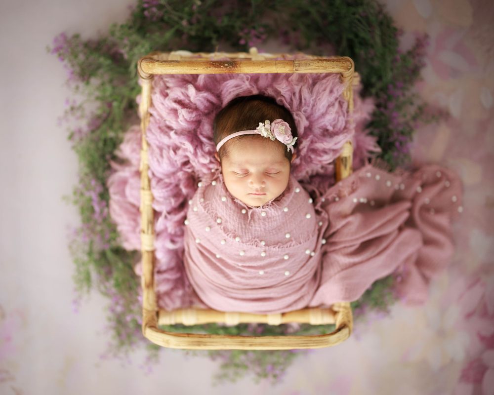 Newborn nestled in pink fabric on vintage wooden frame surrounded by flowers.