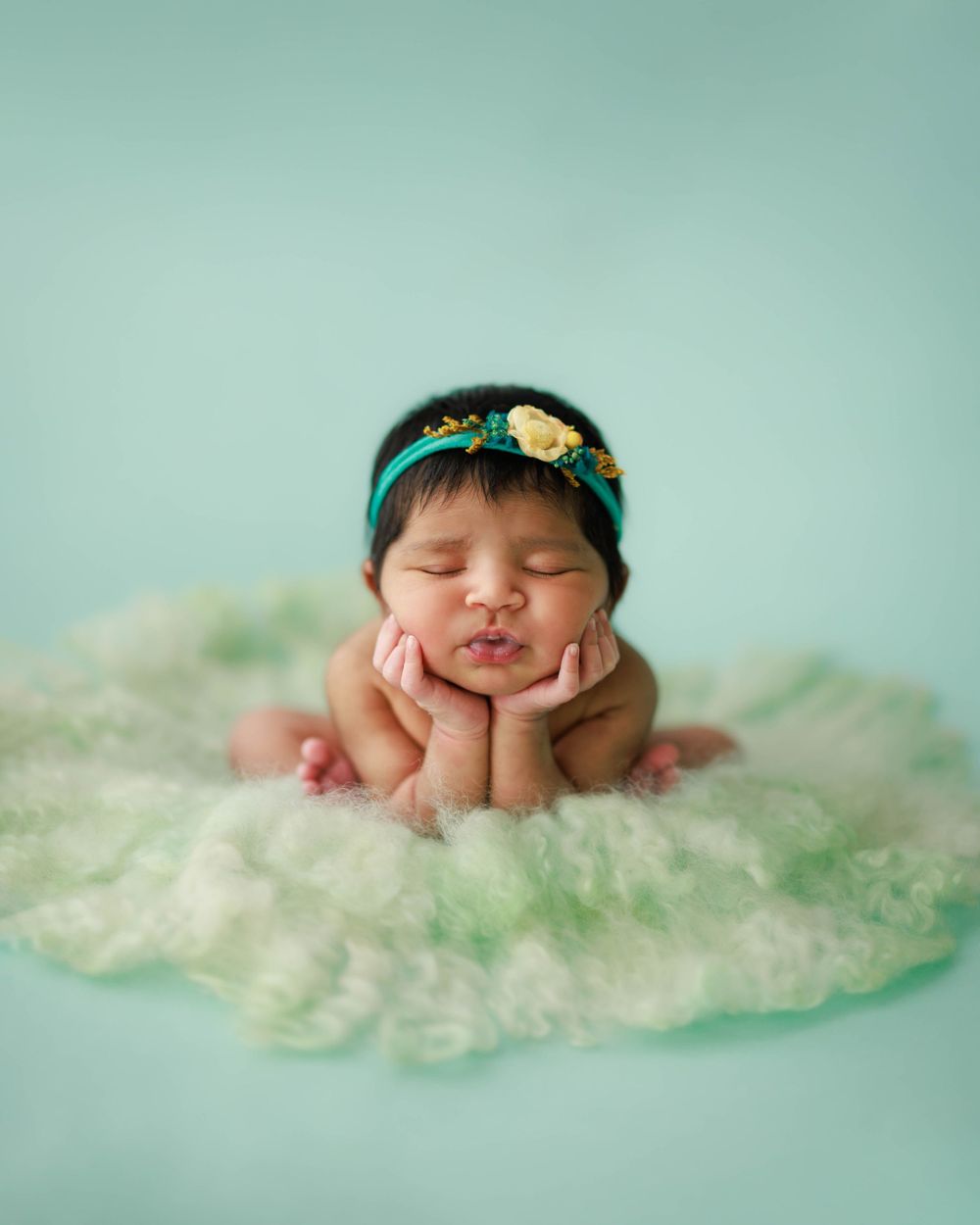 Sleeping newborn with teal headband on mint green cloud-like backdrop.