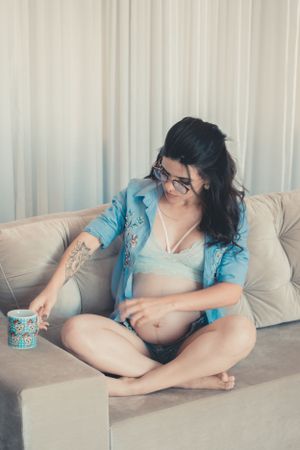 Person relaxing on gray couch wearing blue cardigan with coffee mug in casual home setting.