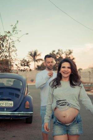 Couple posing playfully by vintage car at sunset with palm trees in background.