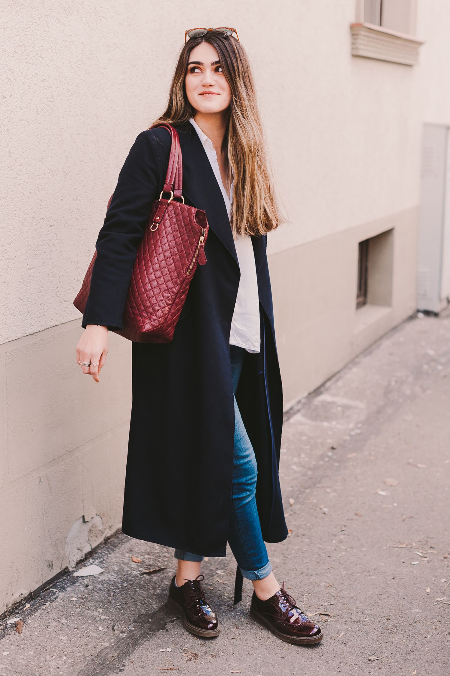 Fashion photo series showing outfit details with black coat and burgundy bag against beige wall.