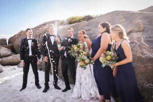 Wedding party in navy and white attire posing on rocky coastal terrain.