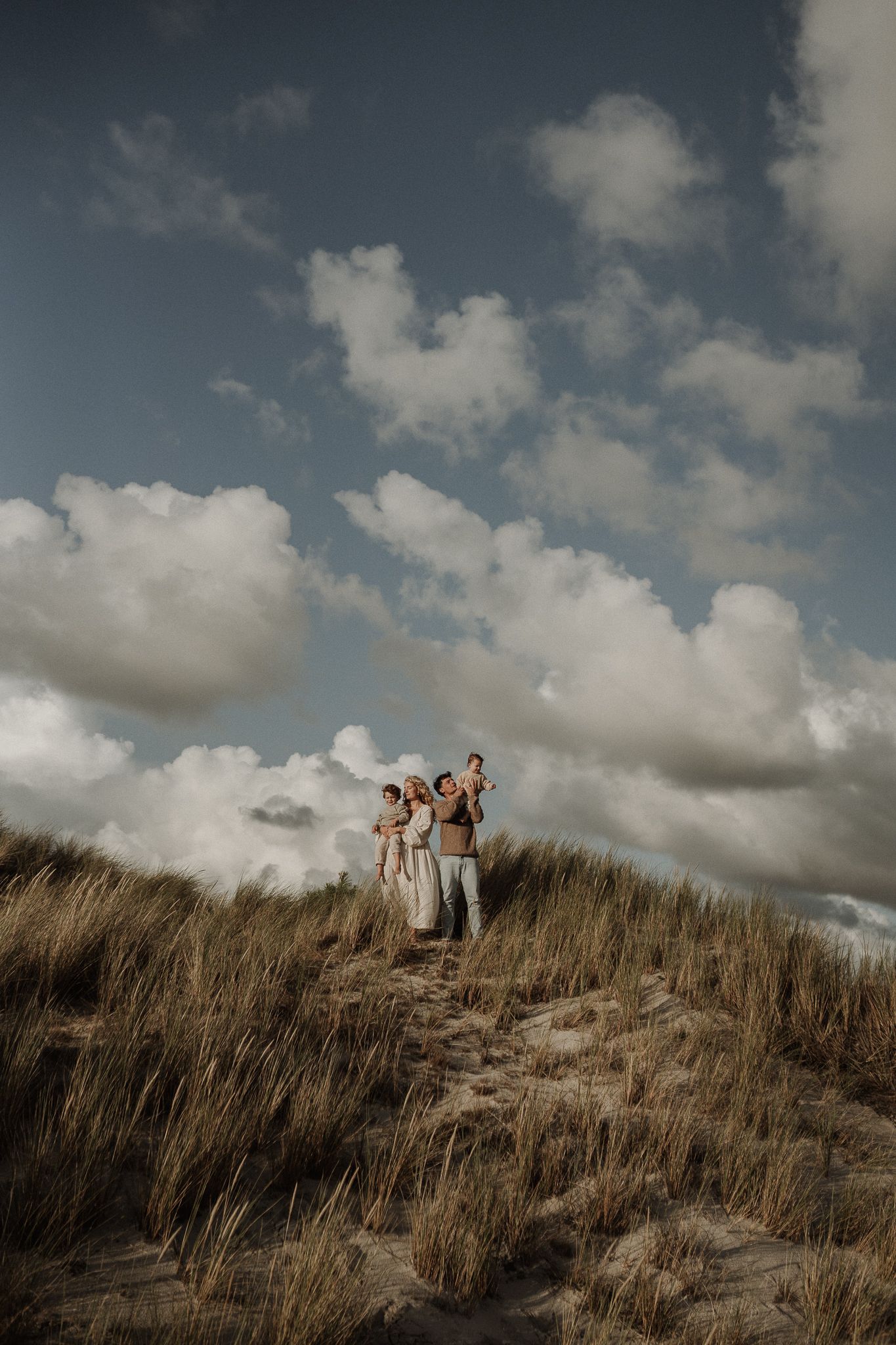 A family stands together on a grassy sand dune against a dramatic cloudy sky.