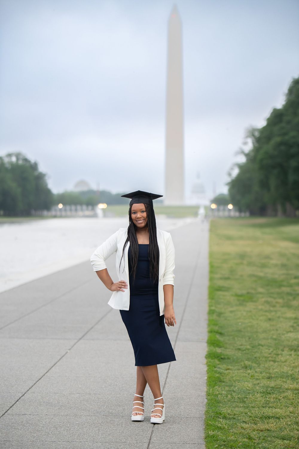 Graduate wearing cap and gown poses near the Washington Monument on the National Mall.