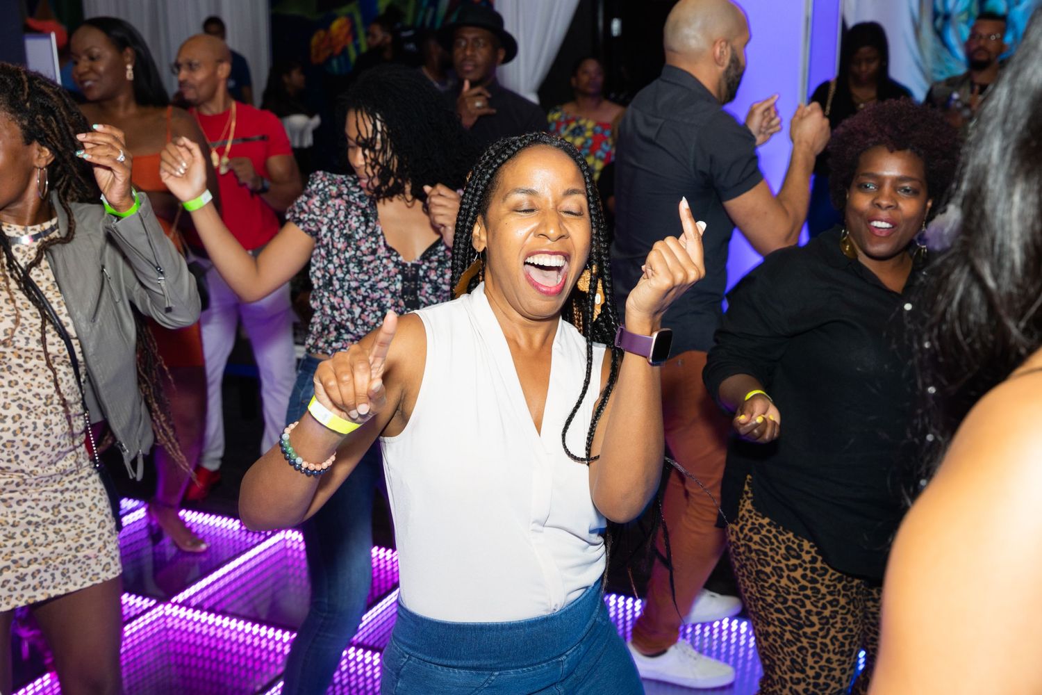 A woman dances energetically on a lit dance floor surrounded by a crowd at a lively party.