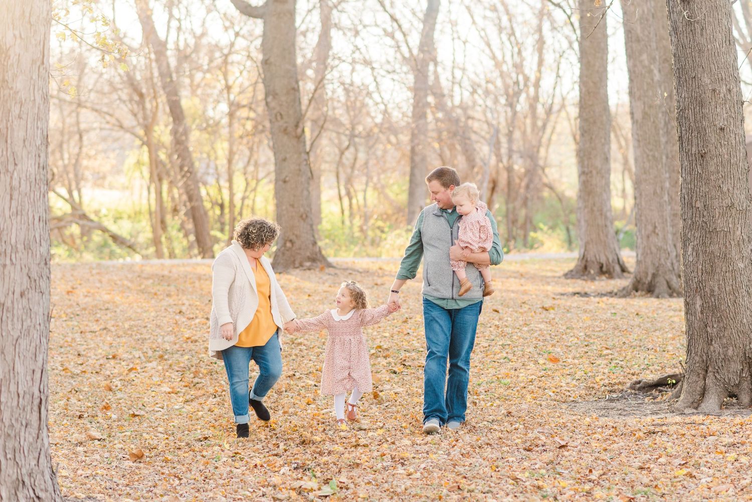 A family walks together through a path covered in fallen autumn leaves.