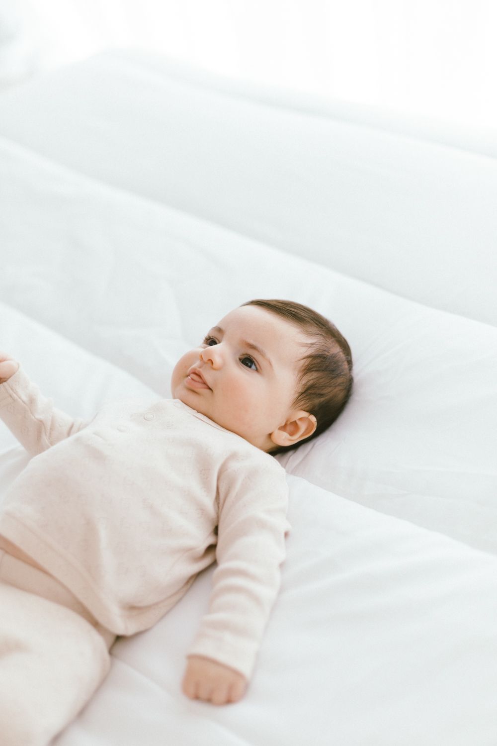 Sweet baby in beige onesie resting peacefully on white bed.