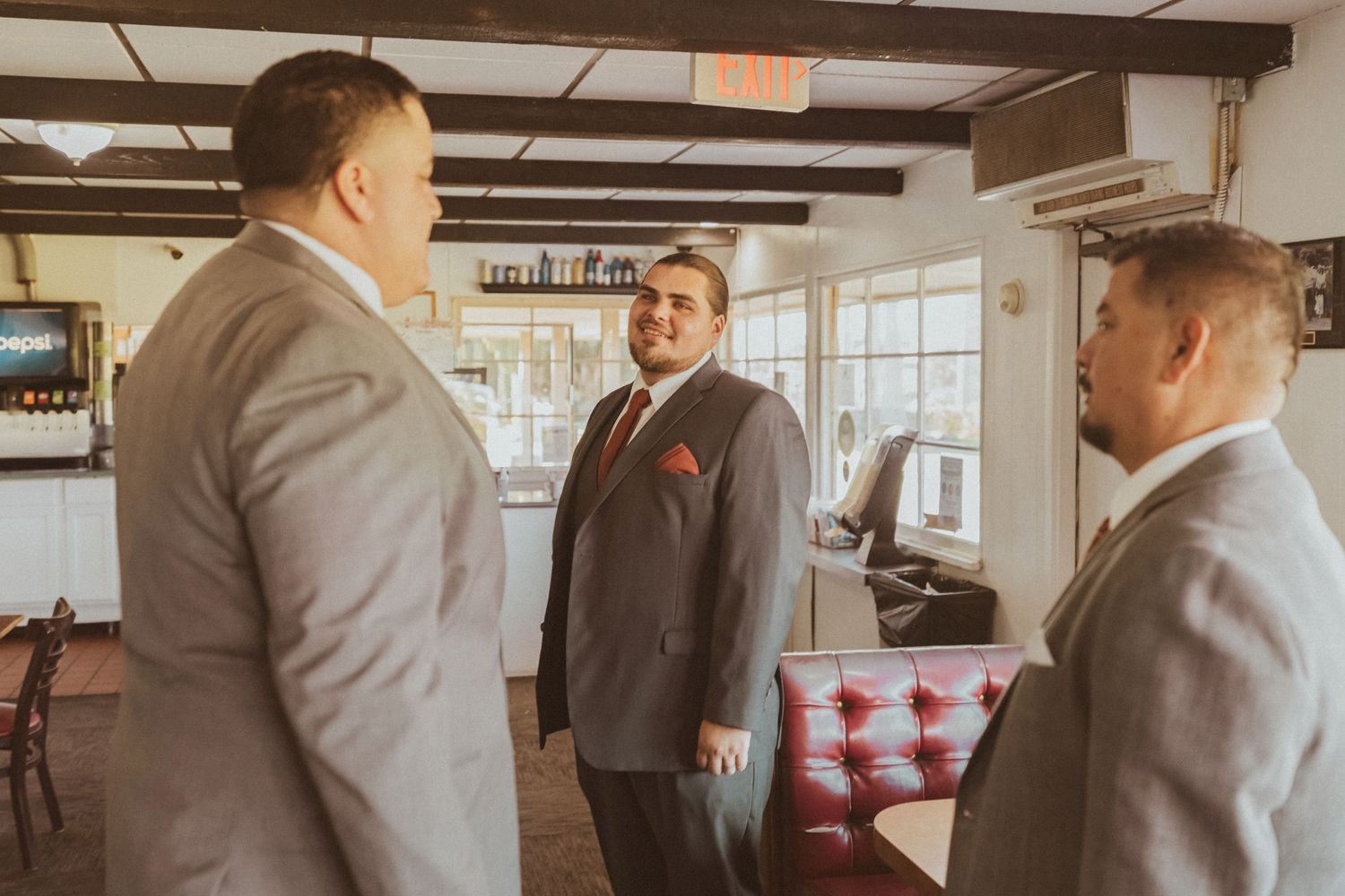 Three people in formal gray suits having a conversation in a rustic room with wooden beams.