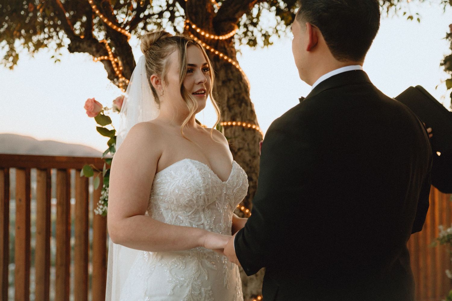 Intimate moment during sunset wedding ceremony with string lights glowing in trees.