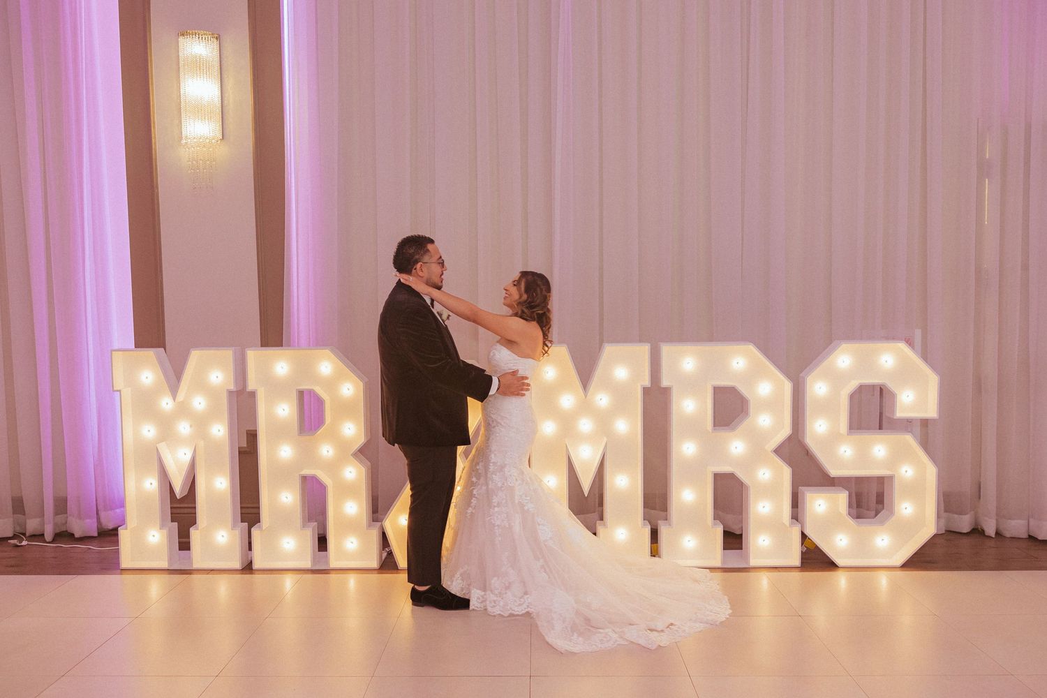 Romantic moment between newlyweds in front of illuminated MR & MRS marquee sign.
