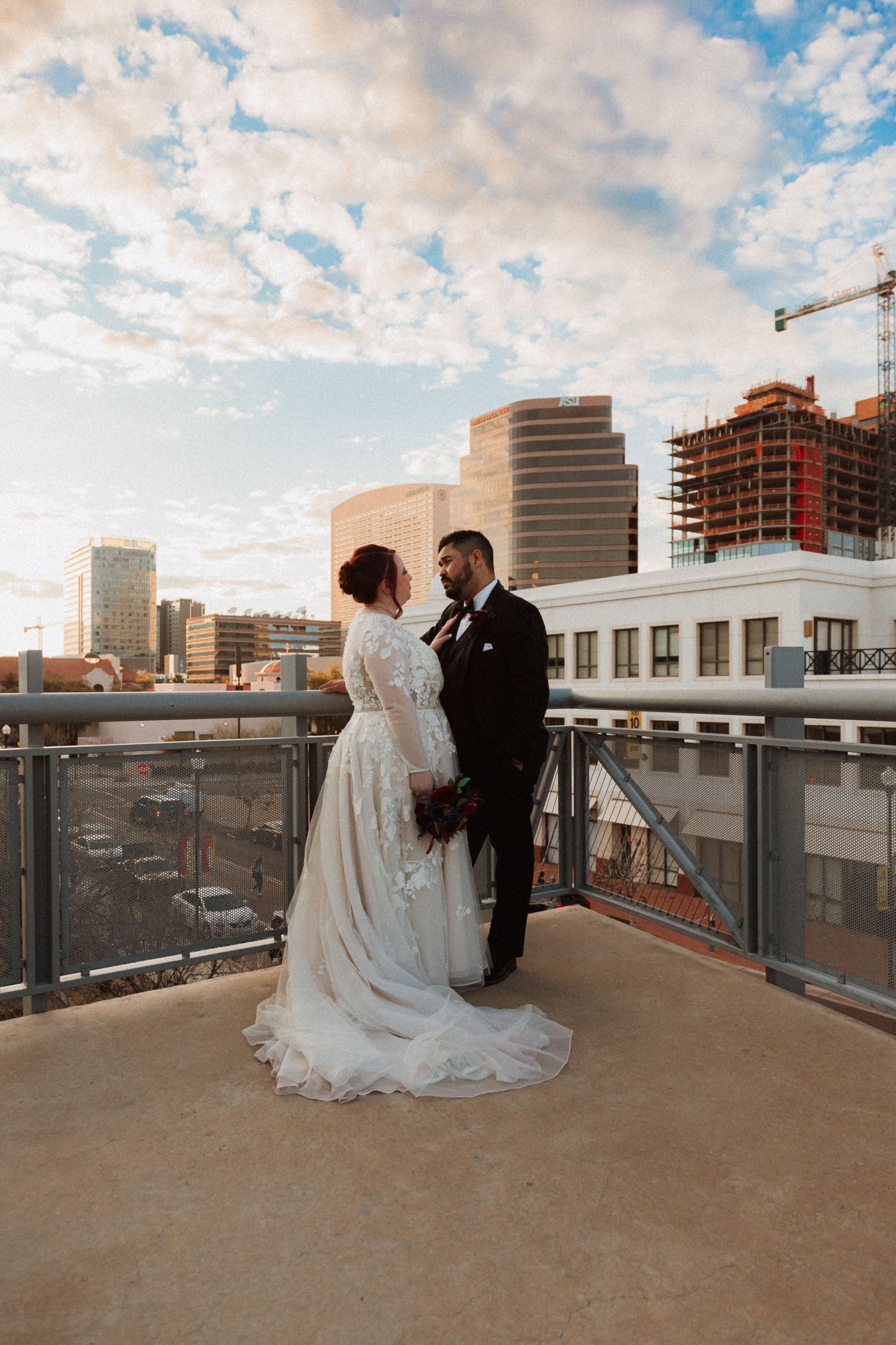 Wedding couple embracing on city rooftop terrace with dramatic cloudy sky behind them.