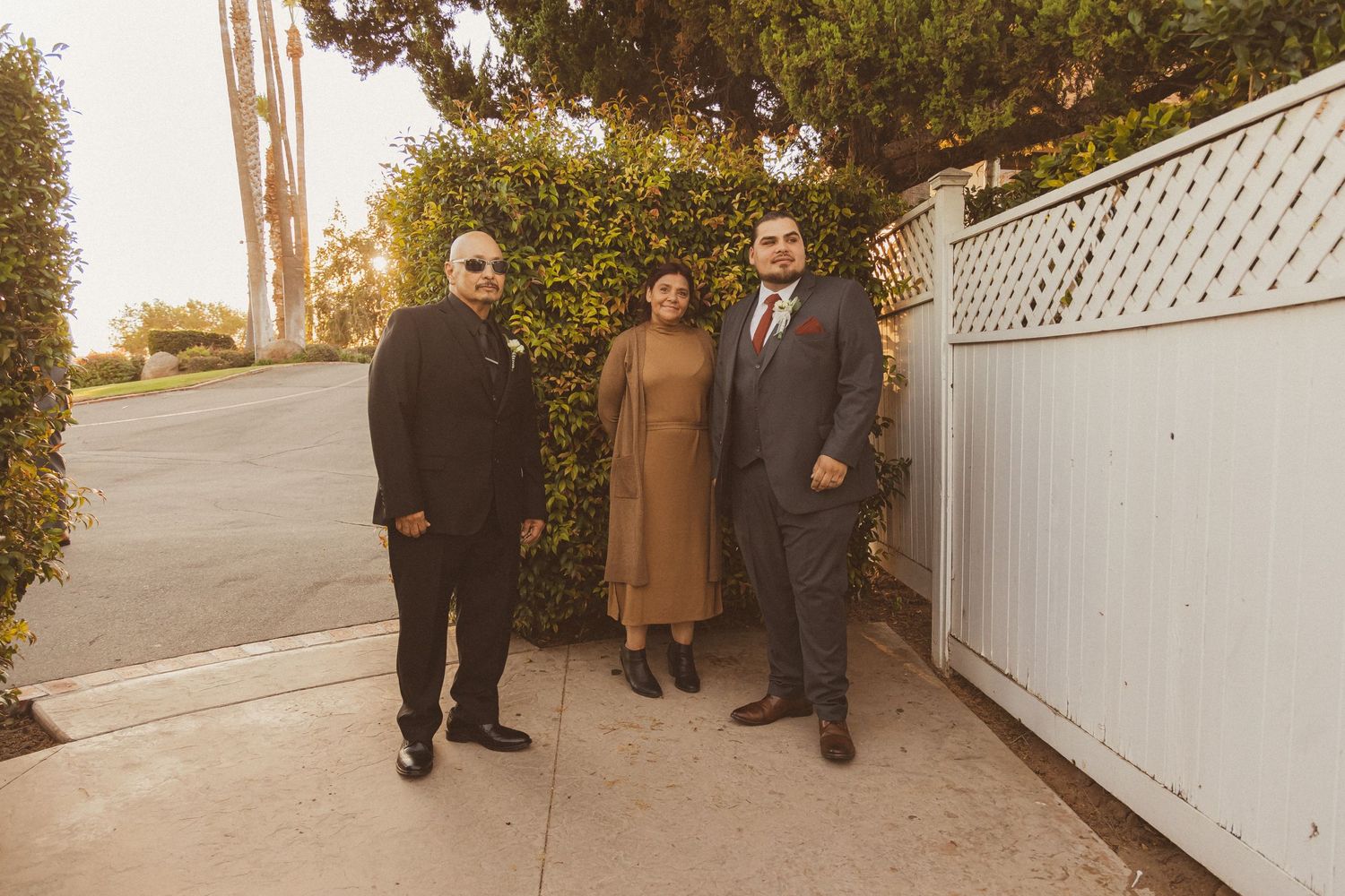 Wedding party members pose together against a white fence during sunset.
