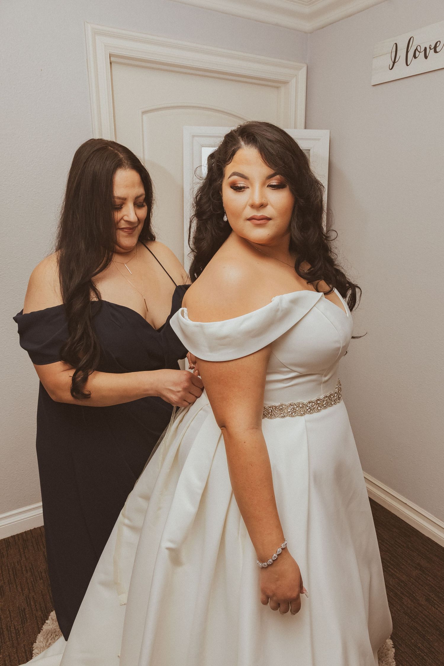 A touching moment during wedding dress preparations with an attendant helping the bride.
