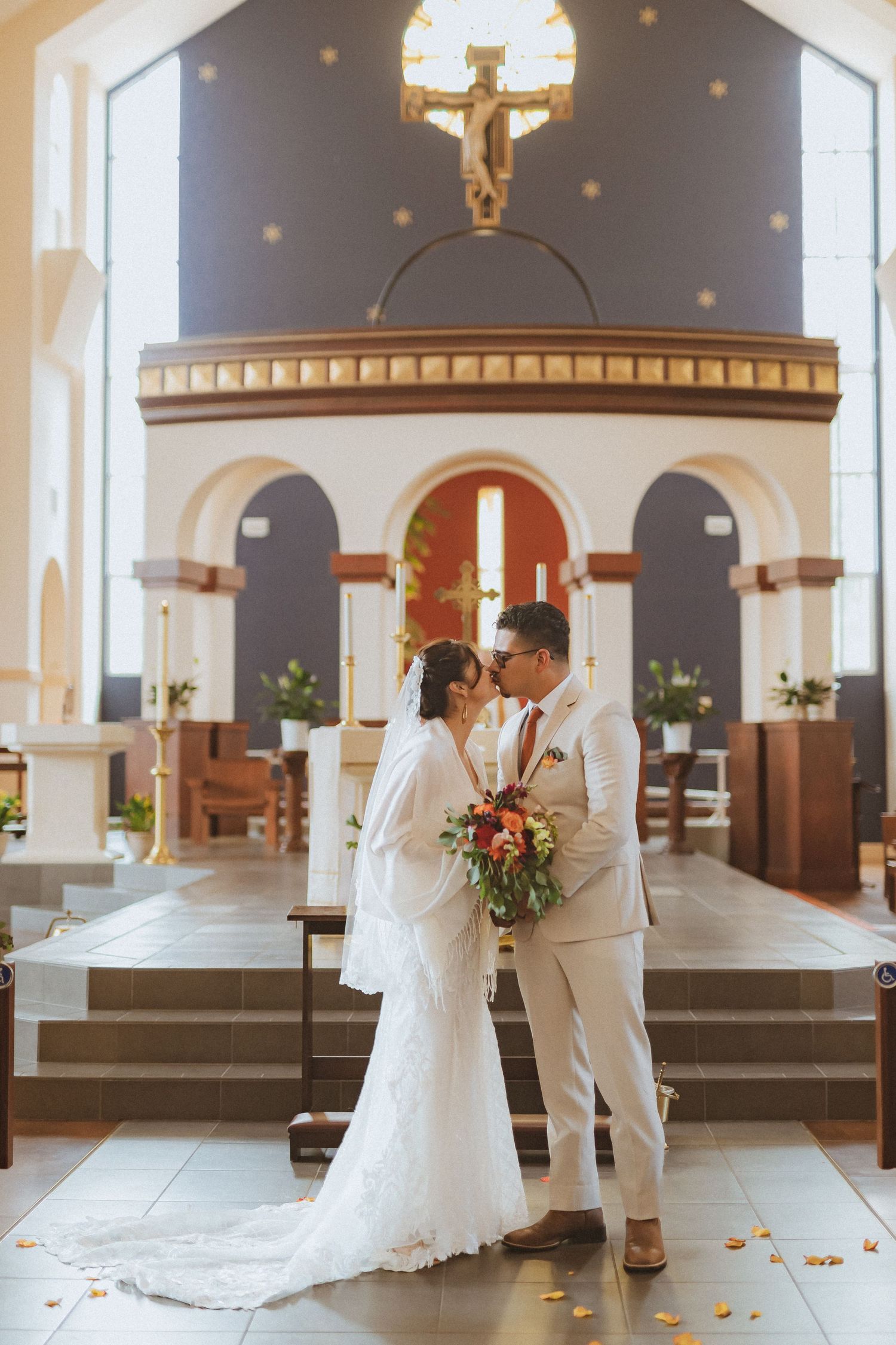 A wedding couple shares an intimate moment at the altar of a Catholic church with a crucifix in the background.
