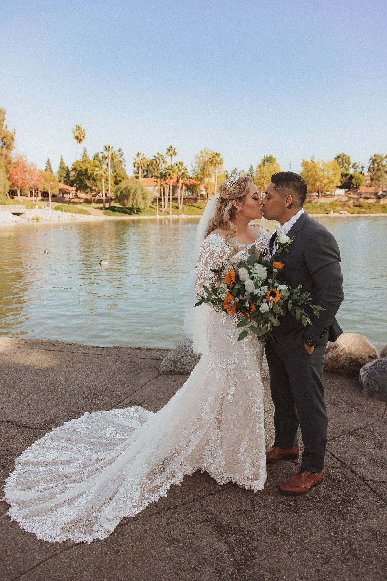 Sunset wedding portrait by the lake with bride's lace dress trailing behind.