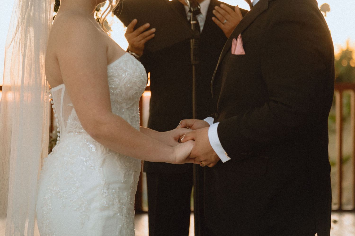 Golden hour wedding ceremony with couple holding hands during vow exchange.