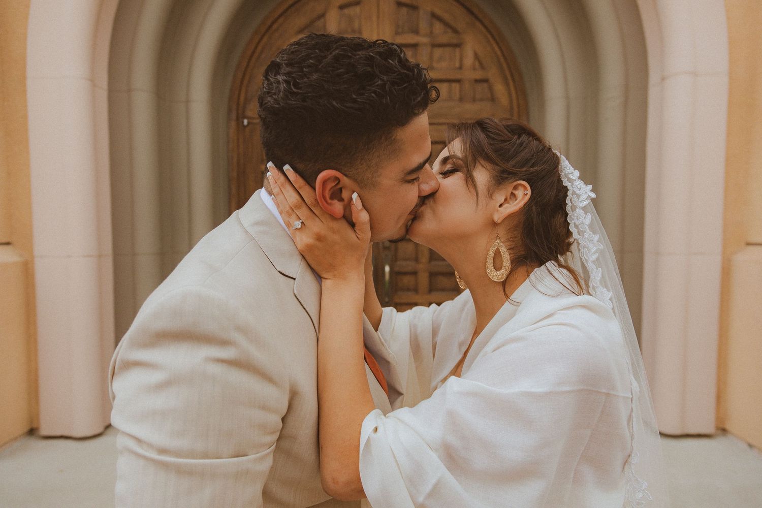 A romantic moment between newlyweds sharing a kiss in front of an arched doorway.