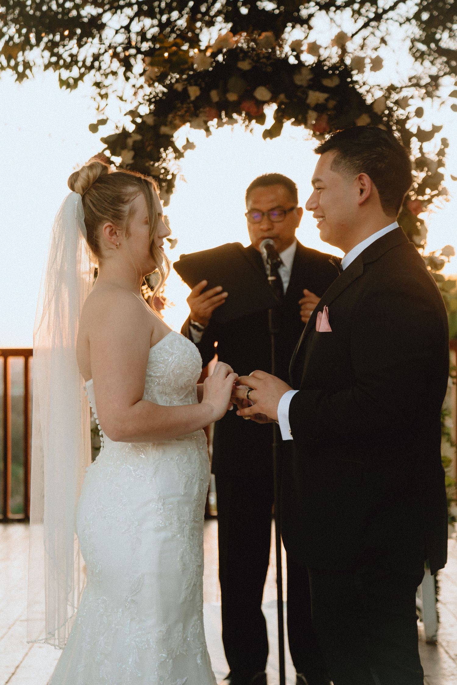 Wedding ceremony captured during ring exchange under an illuminated garden arch.