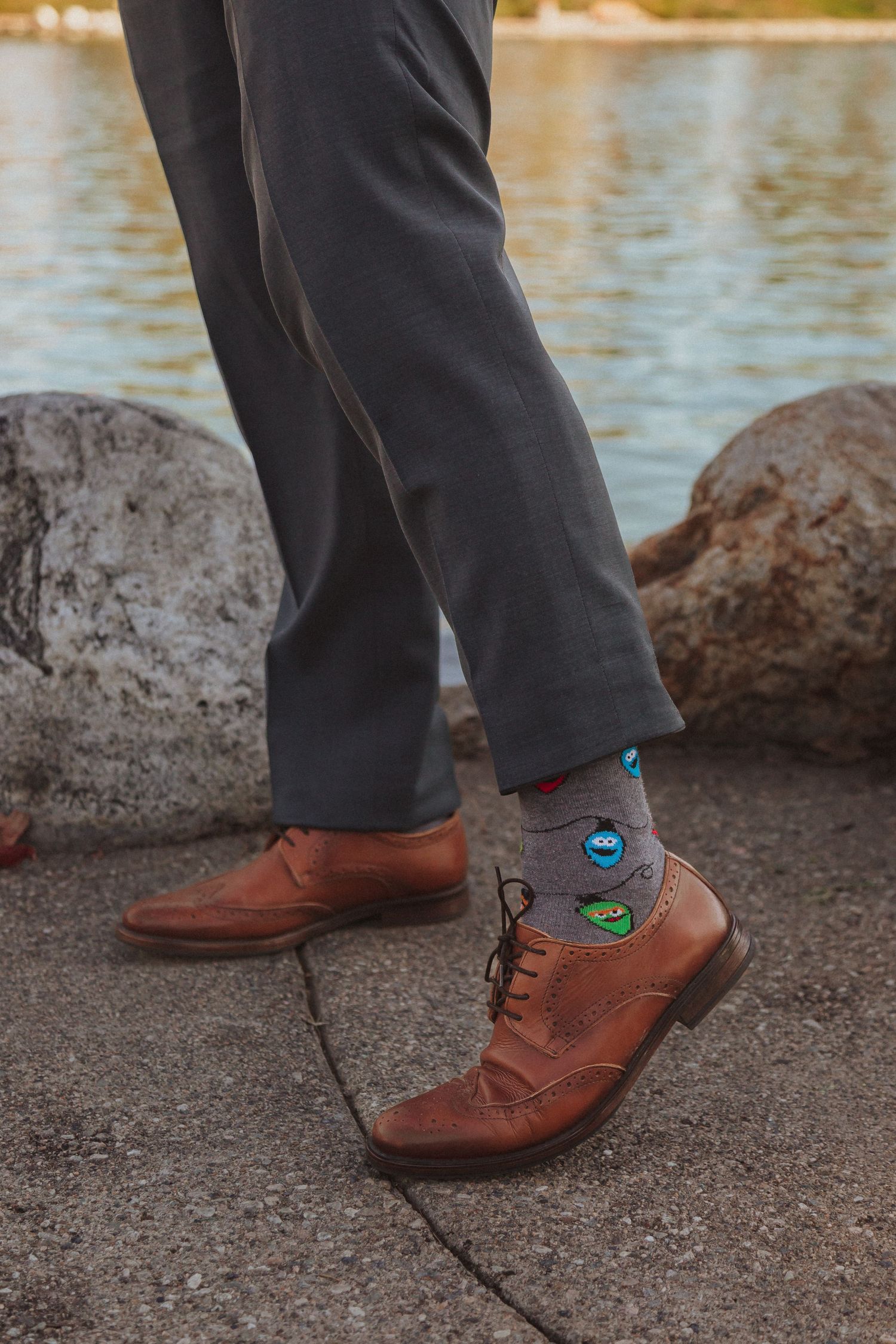 Brown leather dress shoes and fun patterned socks shown against lakeside rocks.
