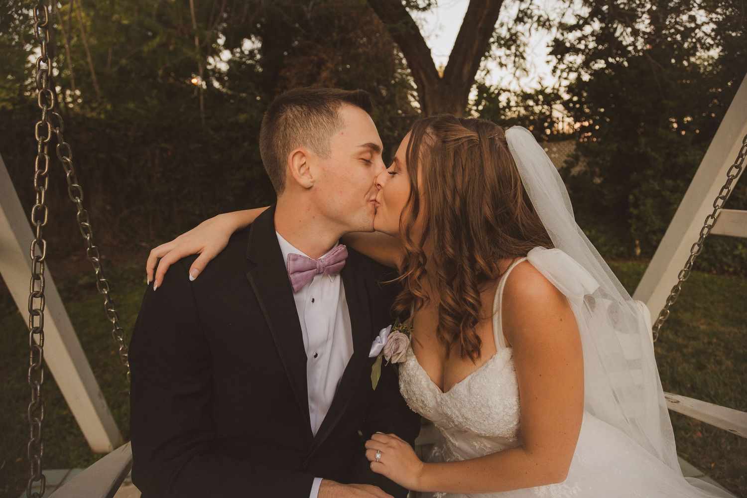 Sunset wedding photo captures romantic kiss between newlyweds outdoors.