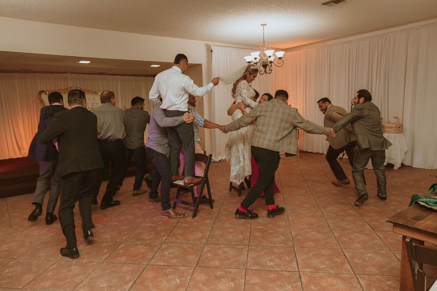 Guests perform coordinated dance moves at a wedding reception with white drapes.