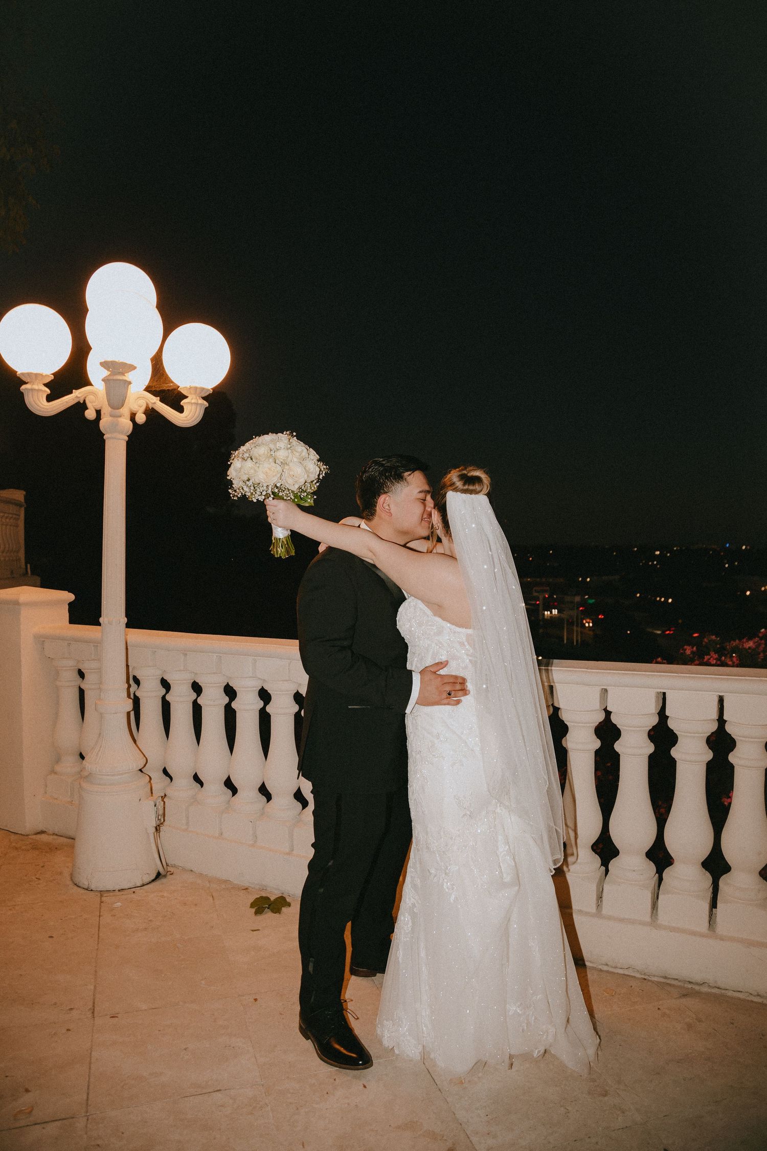 Bride and groom share an intimate dance under illuminated lampposts on a terrace.