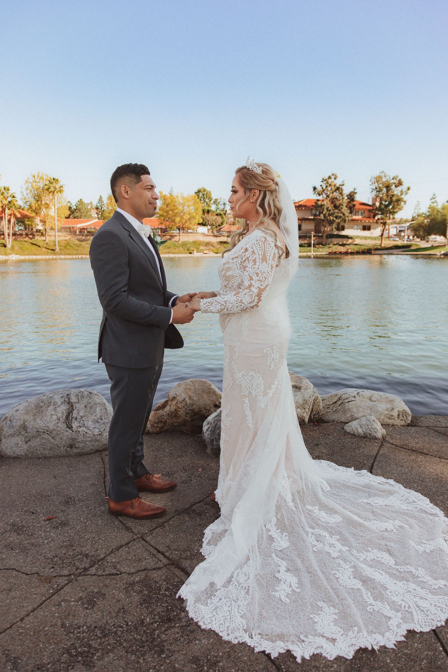 A couple stands by a lakeside while holding hands during their wedding ceremony.