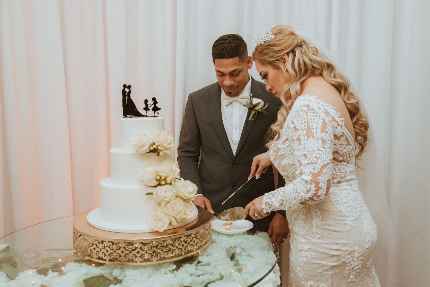 Wedding couple slicing their classic white tiered cake together at their reception.