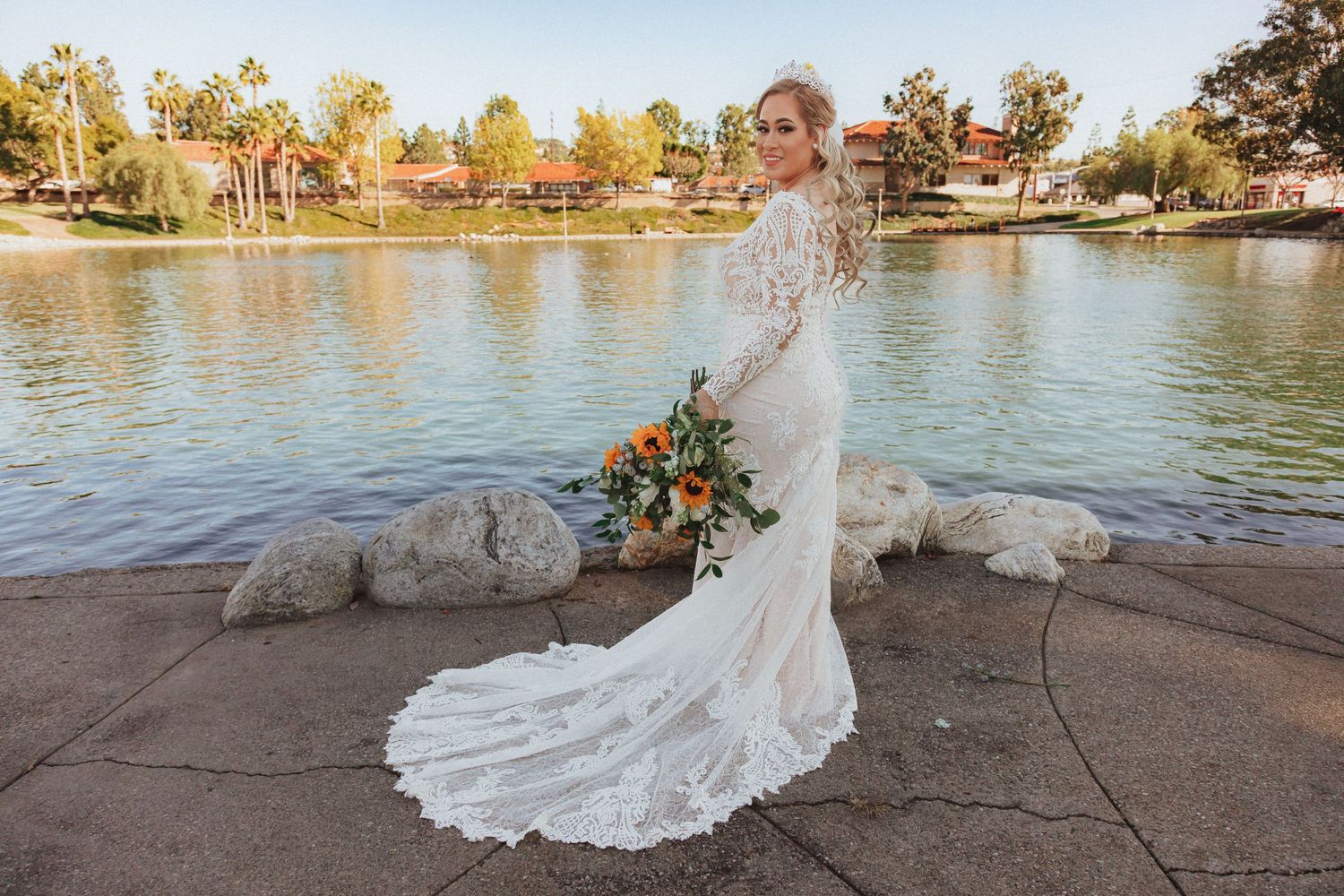 Elegant lace wedding dress with long train photographed near a serene lake at sunset.