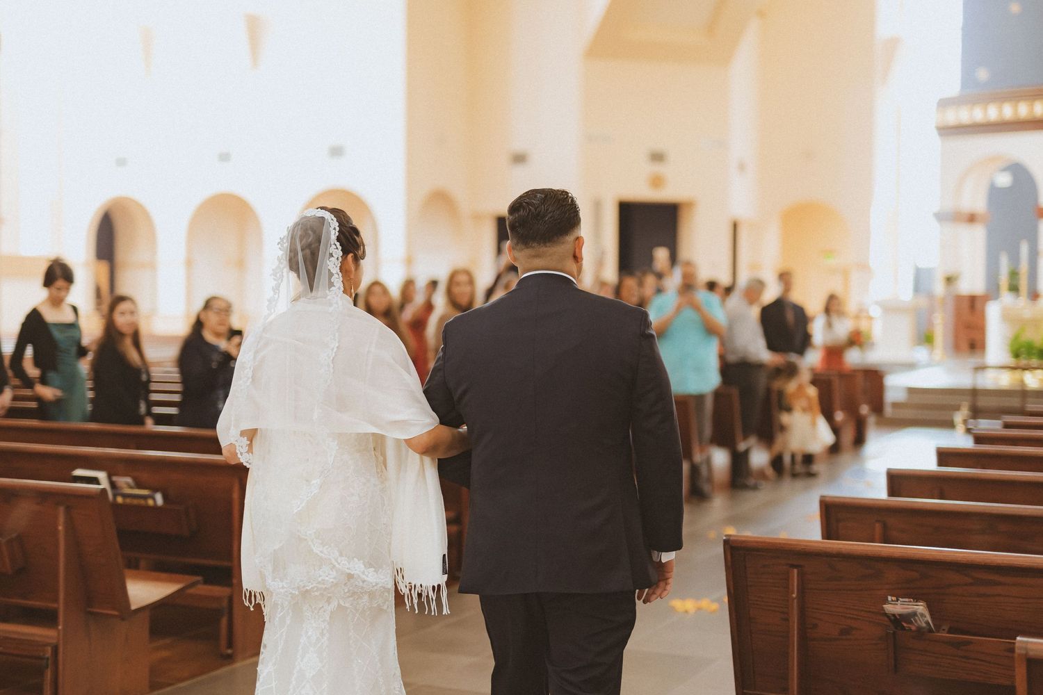 Wedding couple walks down church aisle surrounded by wooden pews.
