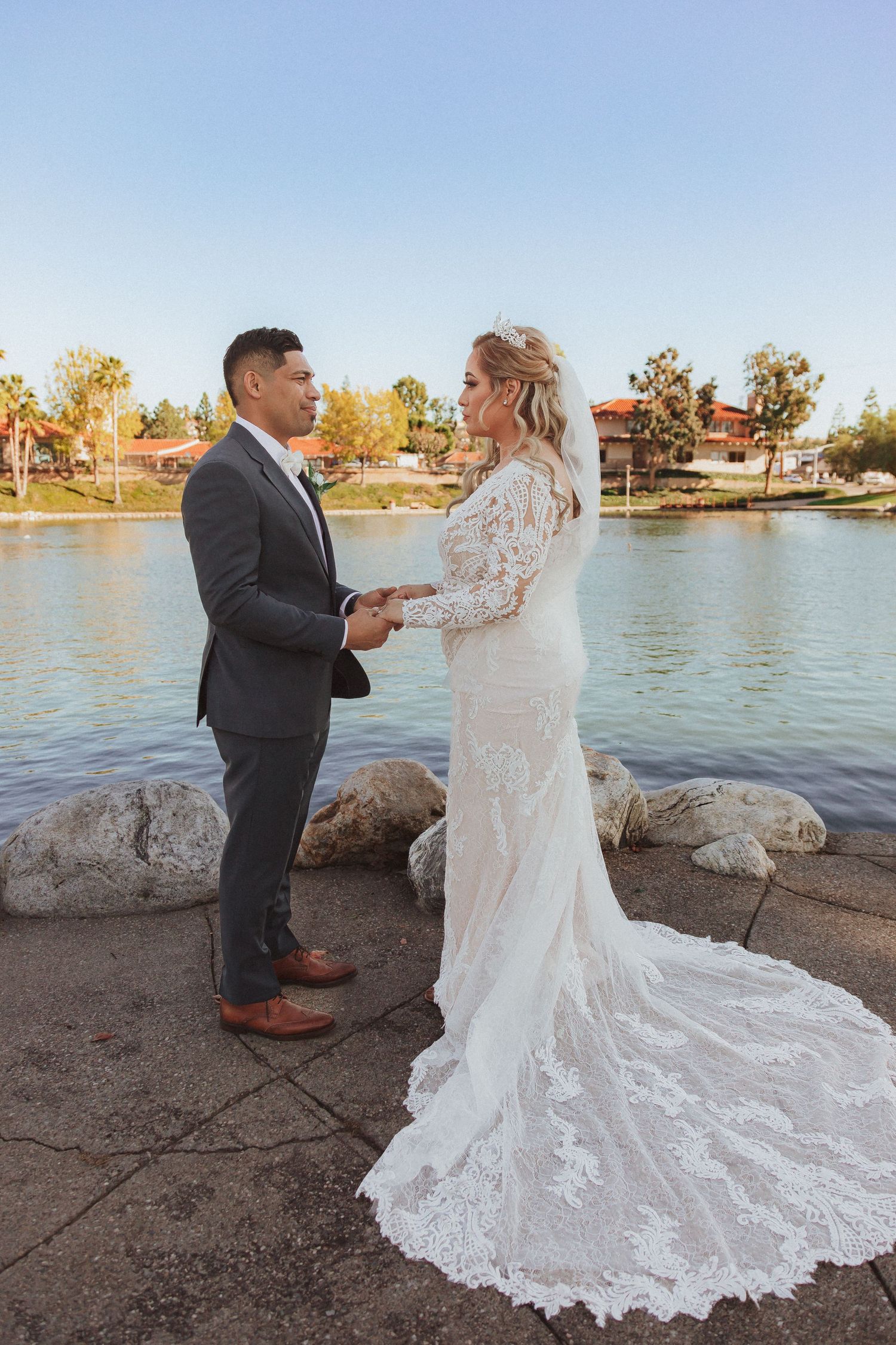 A couple exchanges vows during a waterfront wedding ceremony with a lake and autumn trees in the background.