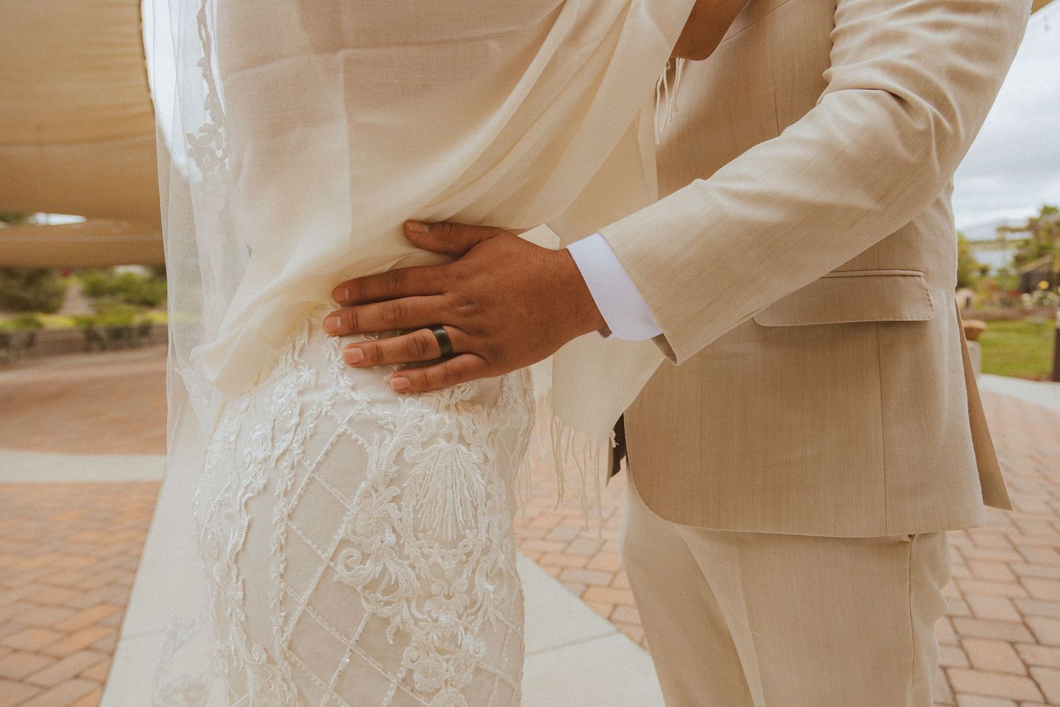 Elegant bridal couple in light beige and white attire holding hands in an intimate moment.