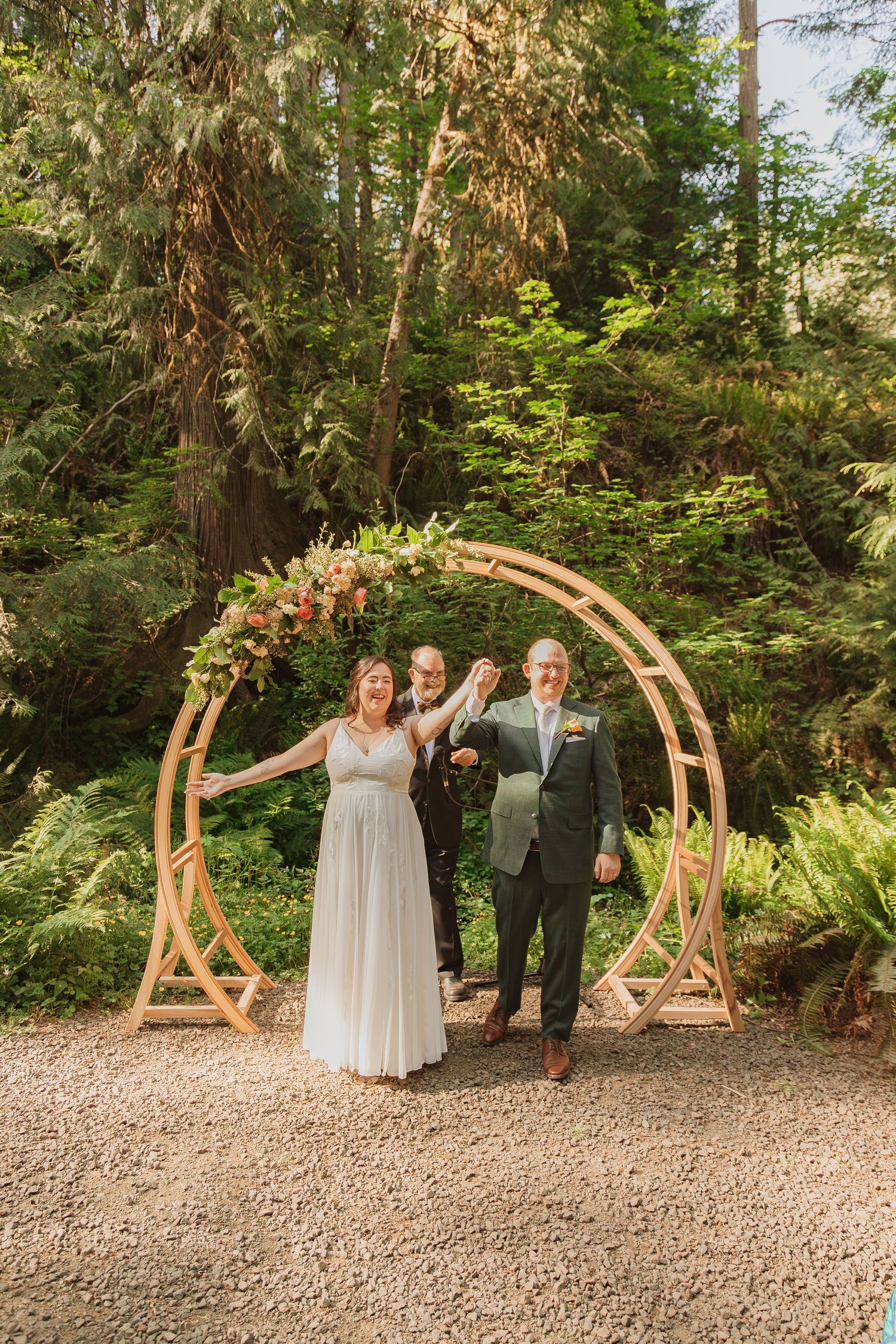 Joyful wedding moment under circular wooden arch decorated with flowers in pacific northwest forest.
