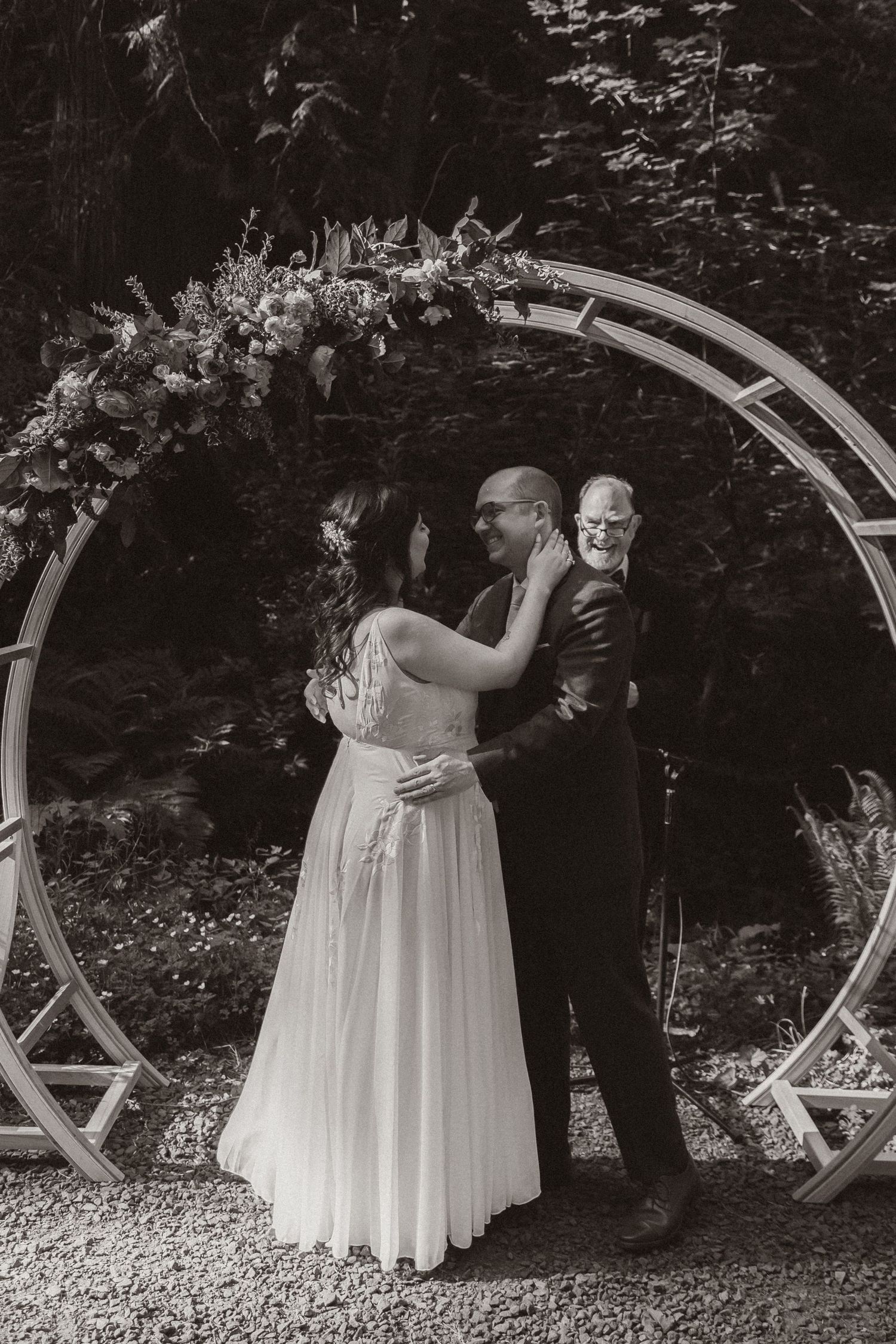 Black and white photo of wedding ceremony moment under circular arch decorated with flowers.