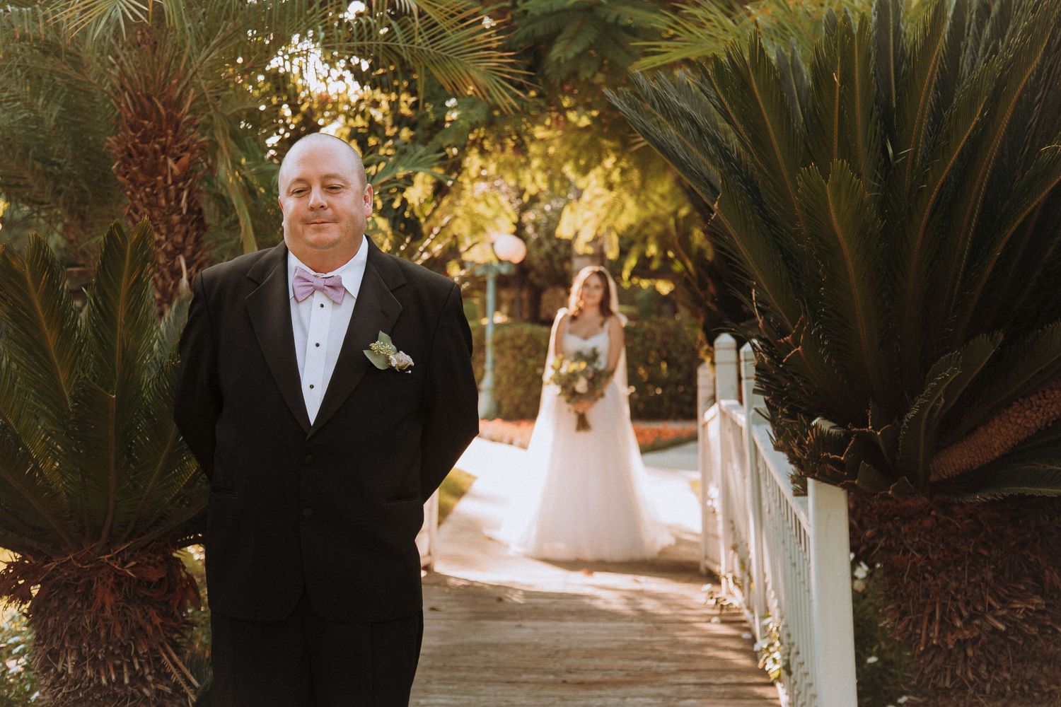 Wedding party member stands on garden path with palms and greenery.