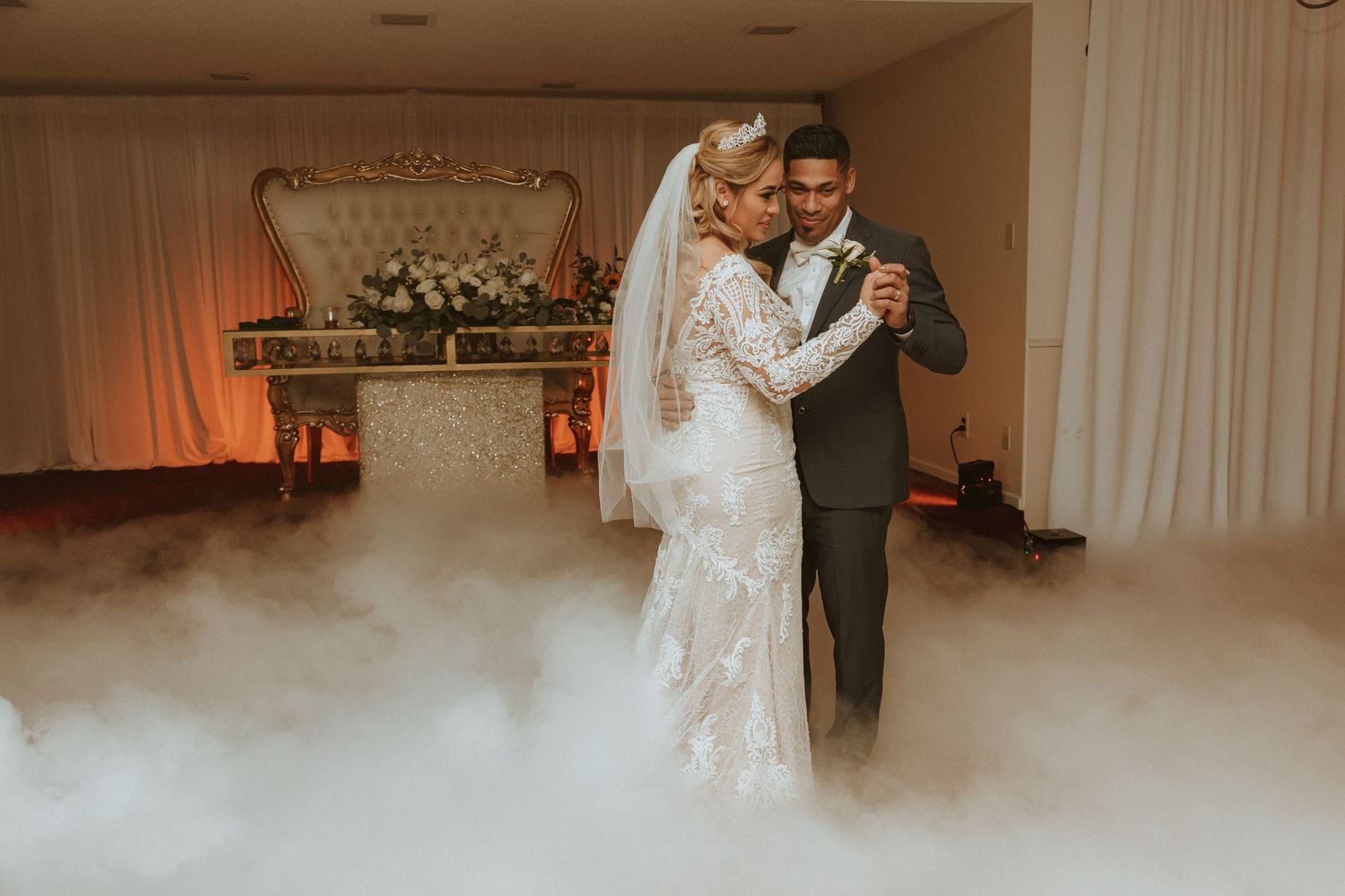 Couple shares intimate dance moment surrounded by elegant decor and atmospheric fog effects.