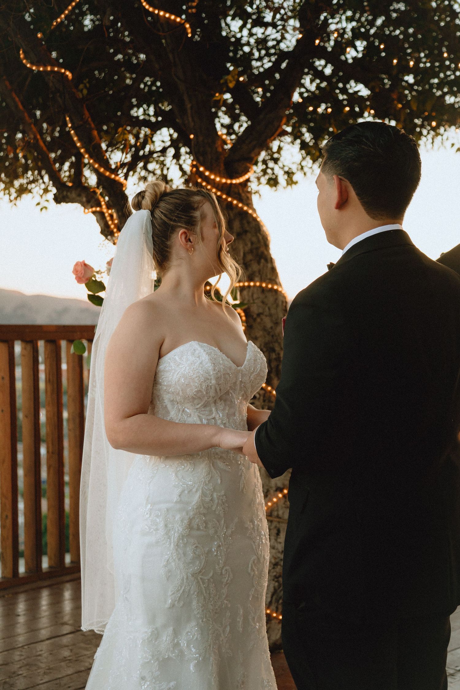 Couple shares wedding vows on wooden deck with string lights and mountain view.