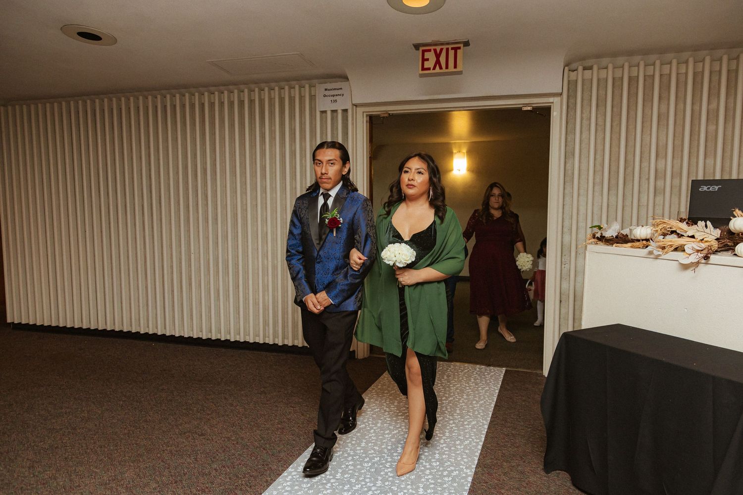 Formal event attendants walk down carpeted aisle during reception entrance.