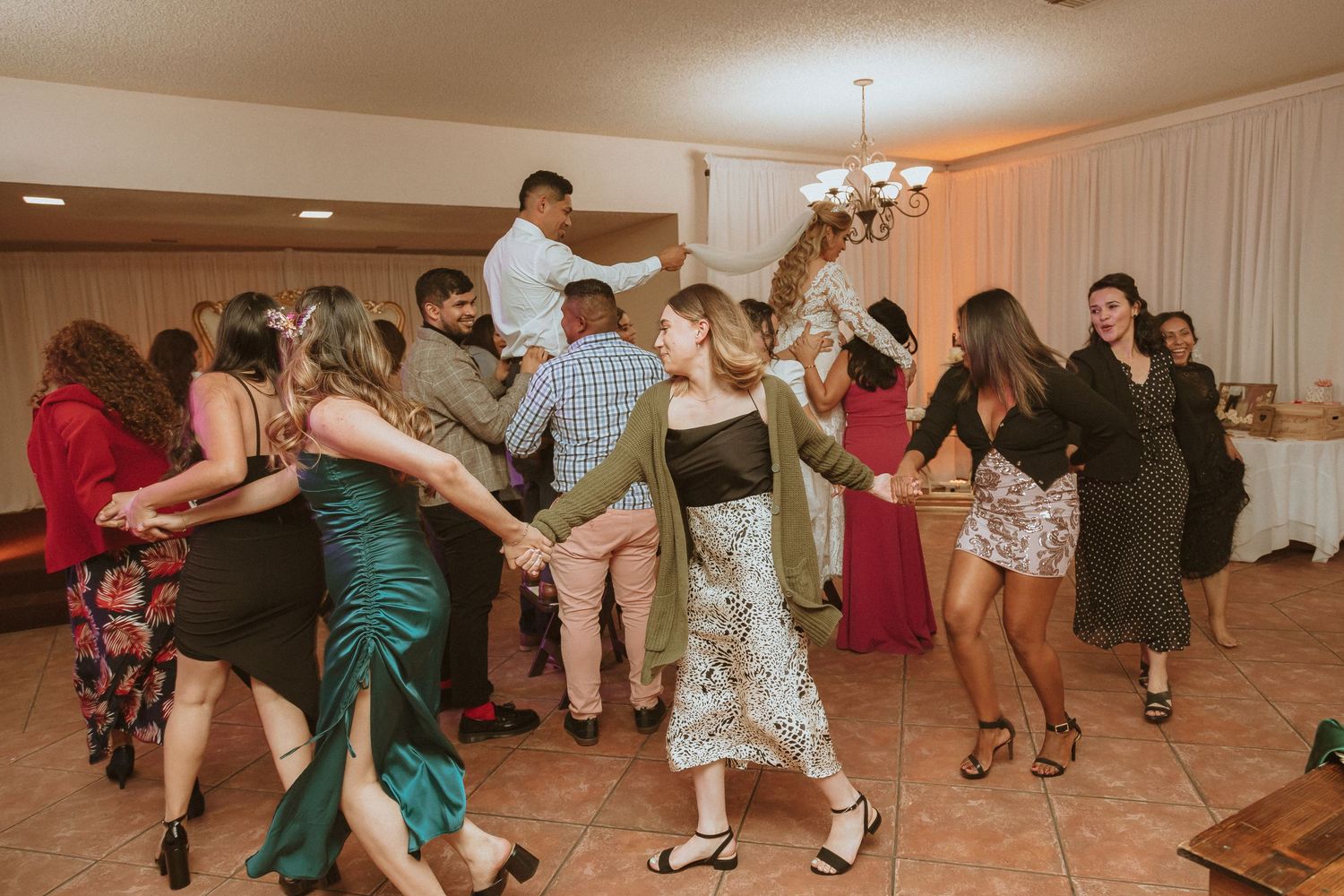 Festive crowd forming a dance circle on a tiled floor at a celebration event.