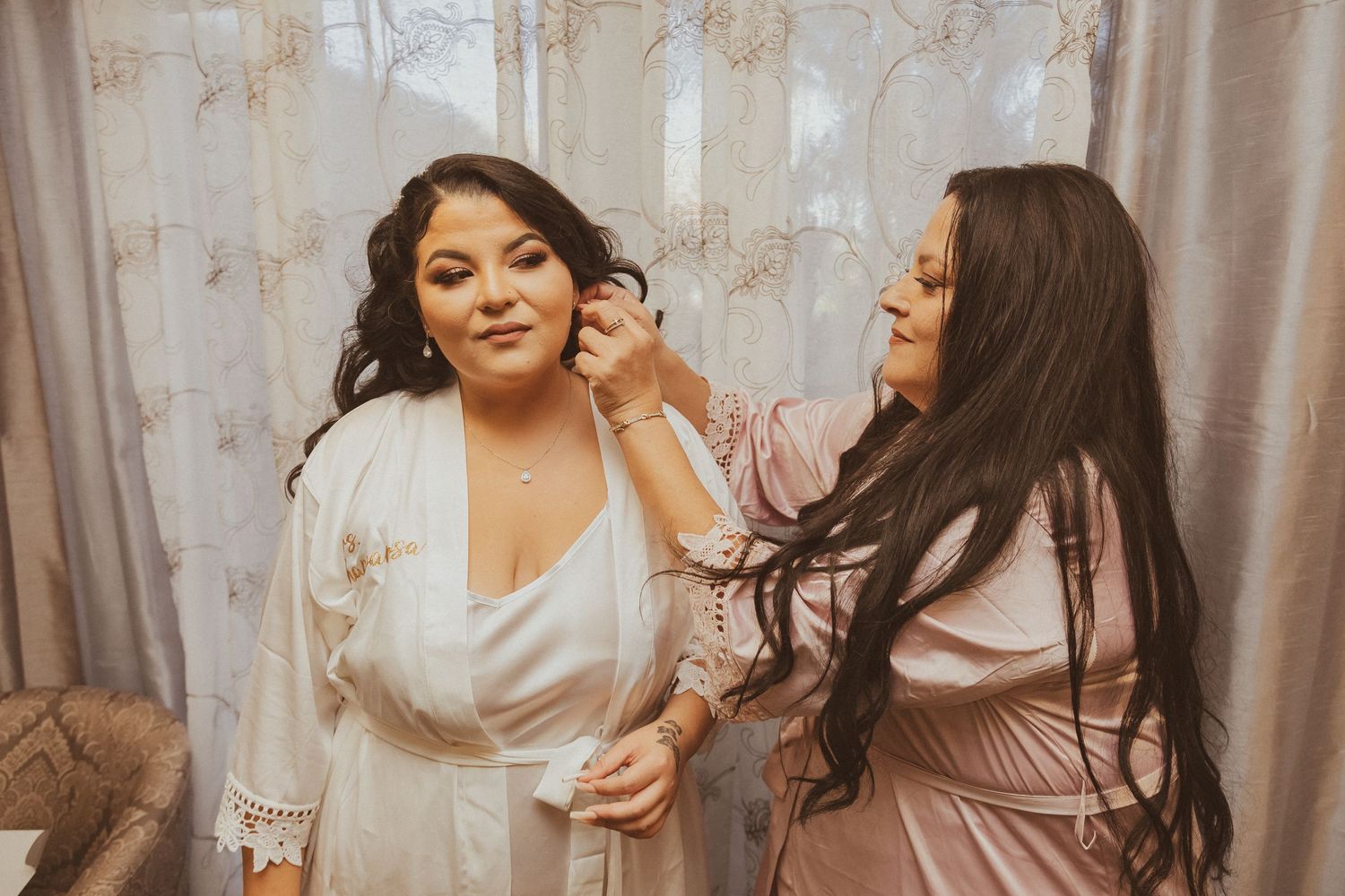 A bridesmaid helps style the bride's curled hair during wedding preparations.