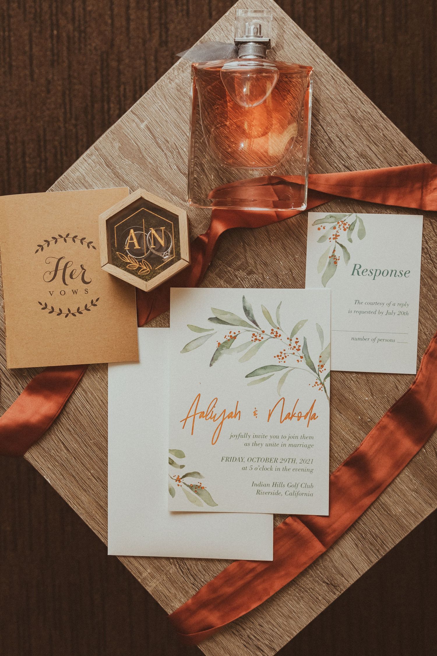 Wedding invitation suite with monogrammed hexagon detail, perfume bottle and terracotta silk ribbon.