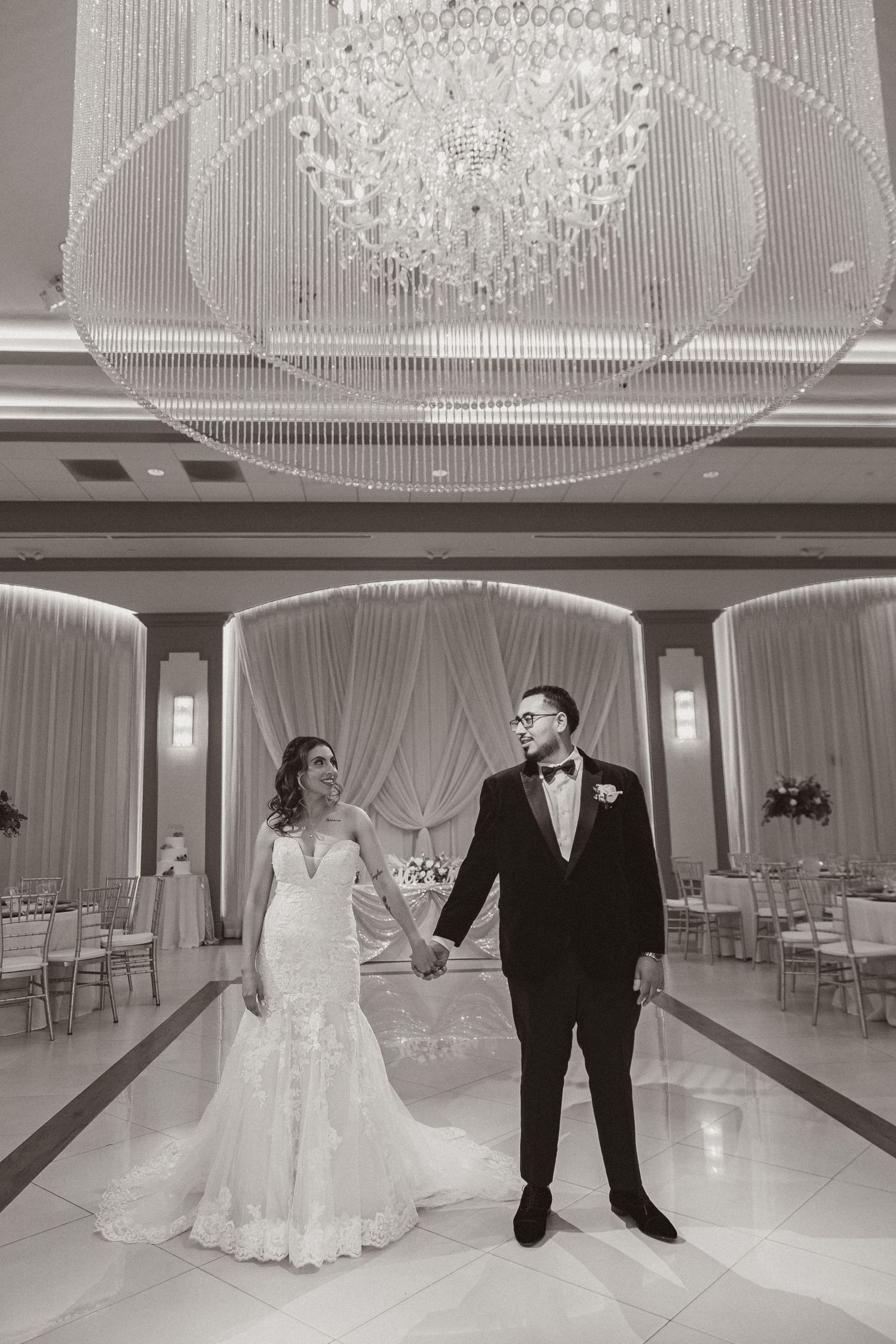 Black and white wedding portrait under a dramatic crystal chandelier in an elegant reception venue.