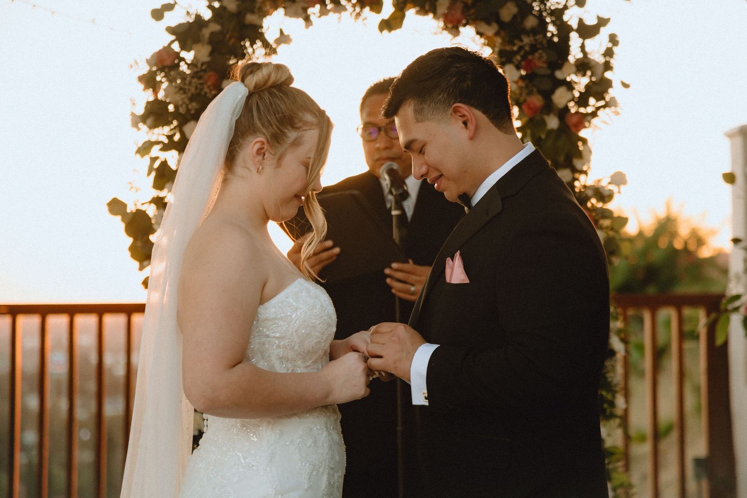 A couple shares an intimate moment during their ring exchange beneath a floral wedding arch.