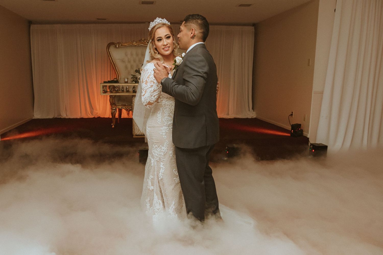Couple dances together in a fog-filled reception venue with warm lighting.