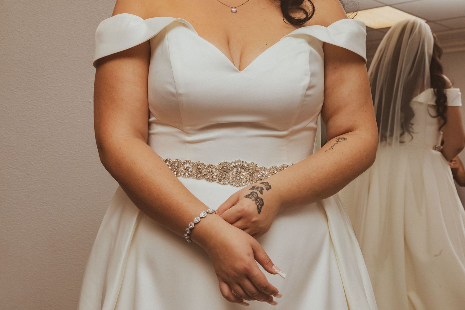 Close-up detail of a white wedding dress with off-shoulder neckline and beaded waistline detail.