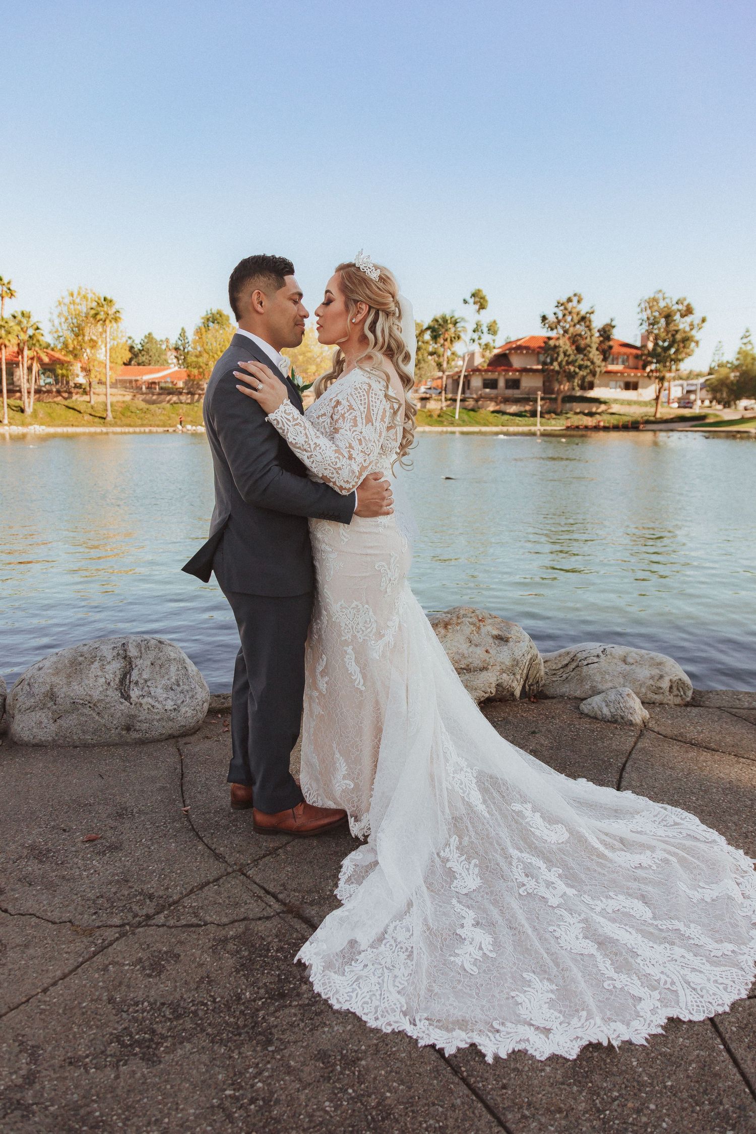 A couple embraces during their lakeside wedding with a beautiful lace gown trailing behind.