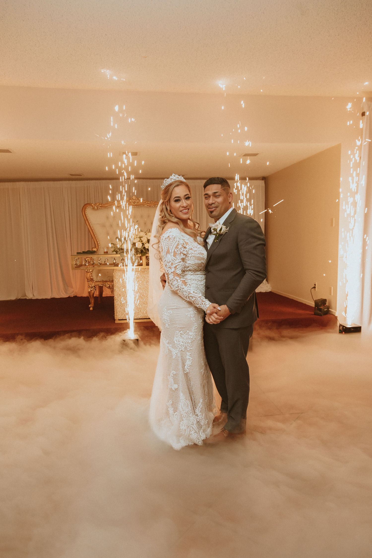 Wedding couple poses between sparkling fountains with dramatic fog effects at their reception.